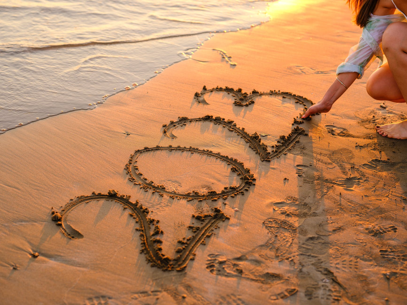 a woman writing numbers on sand with her hand